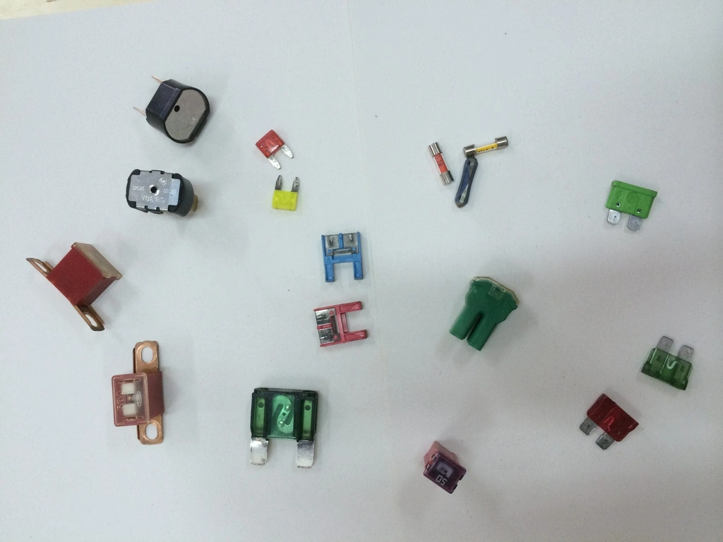 Fusibles automotrices de distintos tipos y colores sobre superficie blanca, organizados por tamaño y amperaje