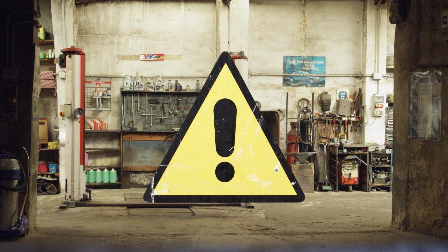 Señalización de seguridad en taller de electromecánica automotriz con señal triangular de advertencia que alerta sobre riesgos mecánicos, eléctricos y electrónicos.