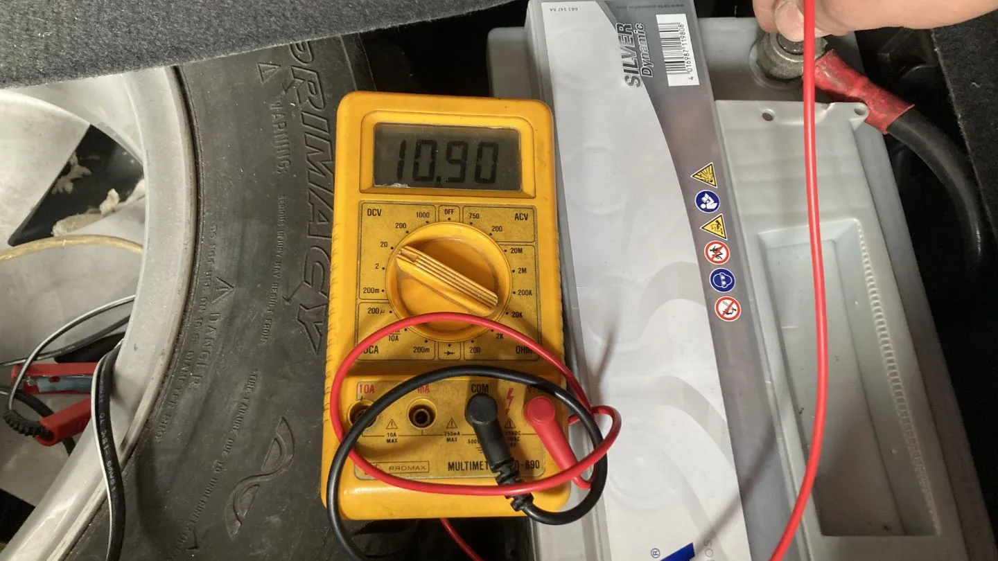 Caída de tensión de la batería durante el arranque del coche mostrando 10.90 voltios en multímetro digital